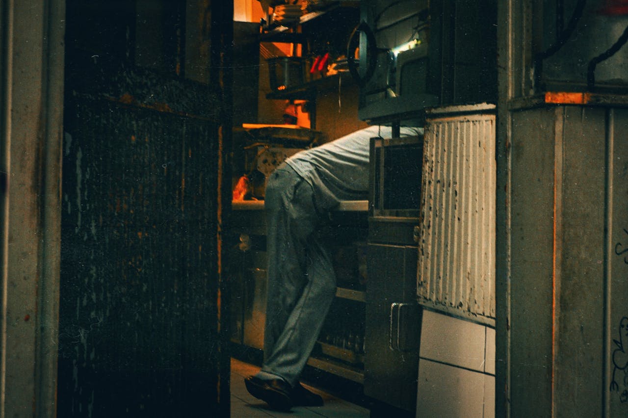 A person in jeans leaning on kitchen equipment in an industrial setting, creating a warm, moody atmosphere.